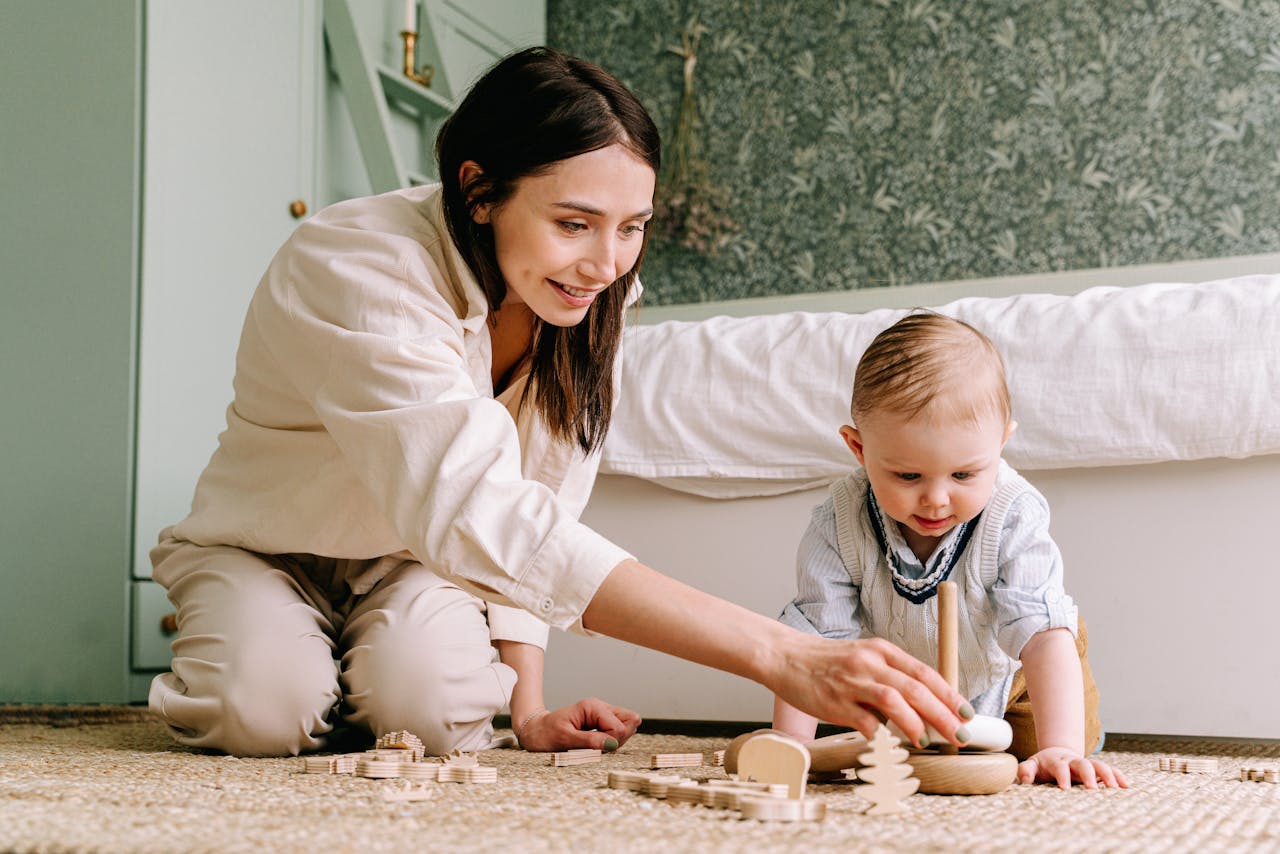 Woman and baby playing with wooden toys on the floor, showcasing love and togetherness indoors.